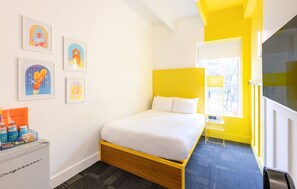 A hotel room with a bed, a desk with a lamp, a window, and artwork on the wall. - The Gallatin(214) Colorful Boutique Hotel (Nashville)