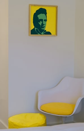 A room with a white chair and a yellow cushion, a framed artwork on the wall, and a yellow ottoman. - The Gallatin(214) Colorful Boutique Hotel (Nashville)