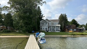 A wooden dock extending into a calm body of water with a house and trees in the background. - 4678 on Glen Lake - Beautiful Luxury Cottage (Maple City)