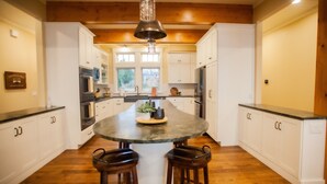 A kitchen with white cabinets, a central island with stools, and a hanging light fixture. - 4678 on Glen Lake - Beautiful Luxury Cottage (Maple City)