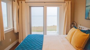 A bedroom with a bed, a view of the sea through a sliding door, and a painting on the wall. - 4678 on Glen Lake - Beautiful Luxury Cottage (Maple City)