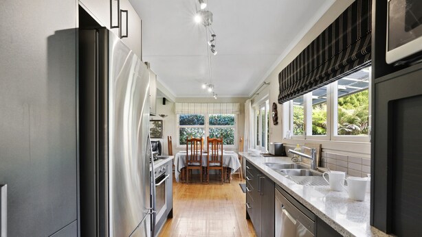 A modern kitchen with stainless steel appliances, a wooden dining table, and a large window providing a view of greenery. - Pukeko Lodge - Tūrangi Holiday Home (Turangi)