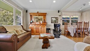 A spacious living room with a leather sofa, wooden cabinet, and a dining area with chairs and a table. - Pukeko Lodge - Tūrangi Holiday Home (Turangi)