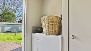 A laundry room with a washing machine and a wicker basket on top. - Pukeko Lodge - Tūrangi Holiday Home (Turangi)