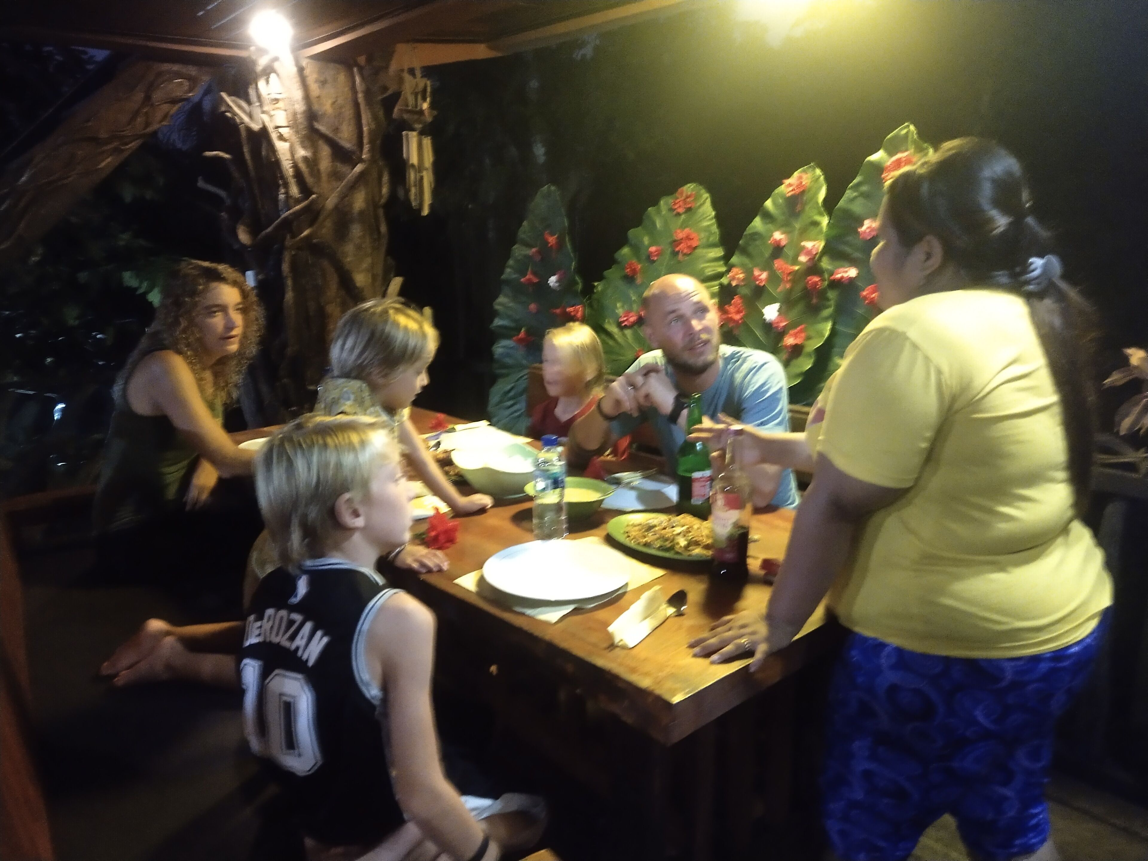 Un grupo de personas sentadas alrededor de una mesa de madera con un plato de comida y una botella de vino.