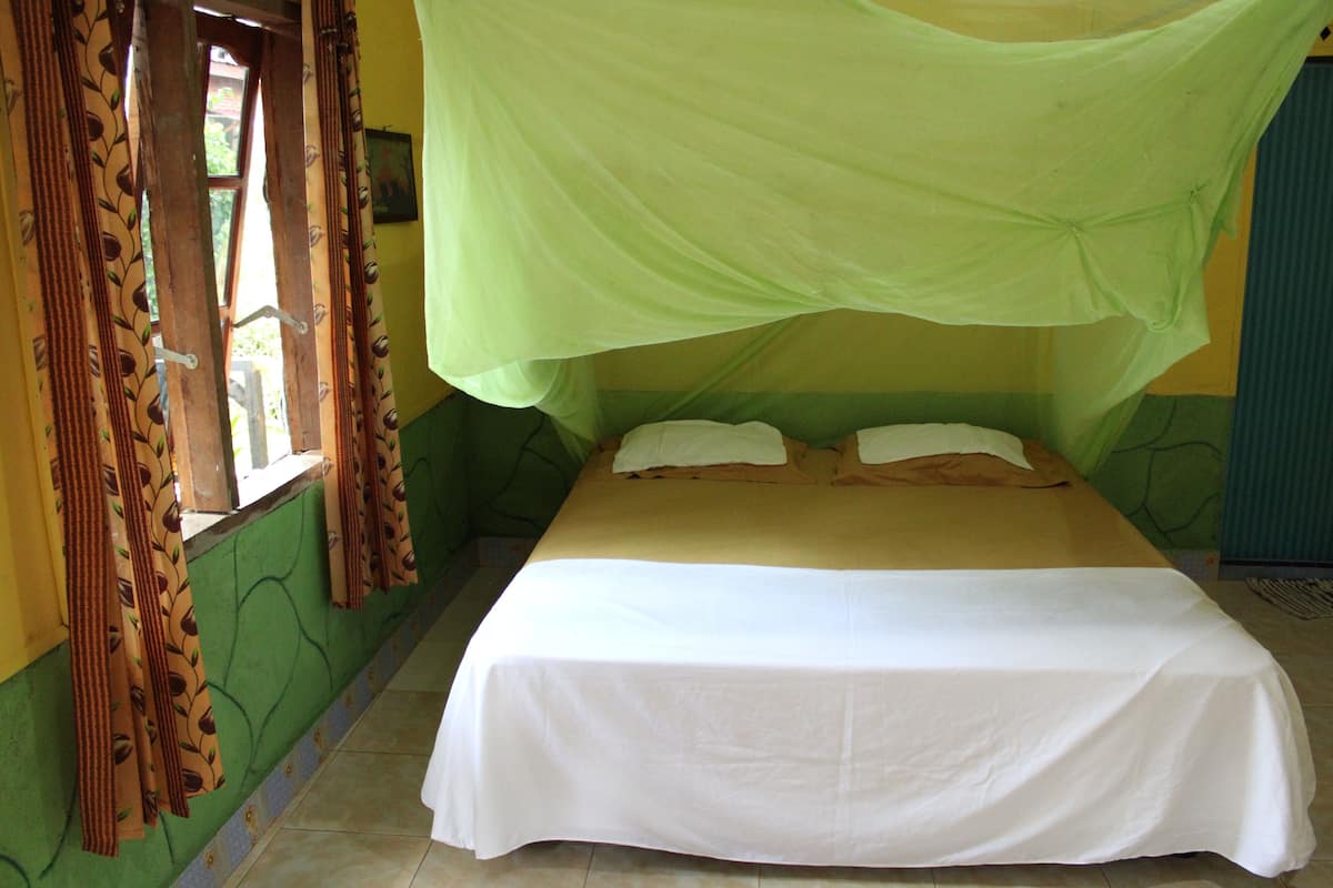 Een enkel bed met een witte sprei en een groen baldakijn.