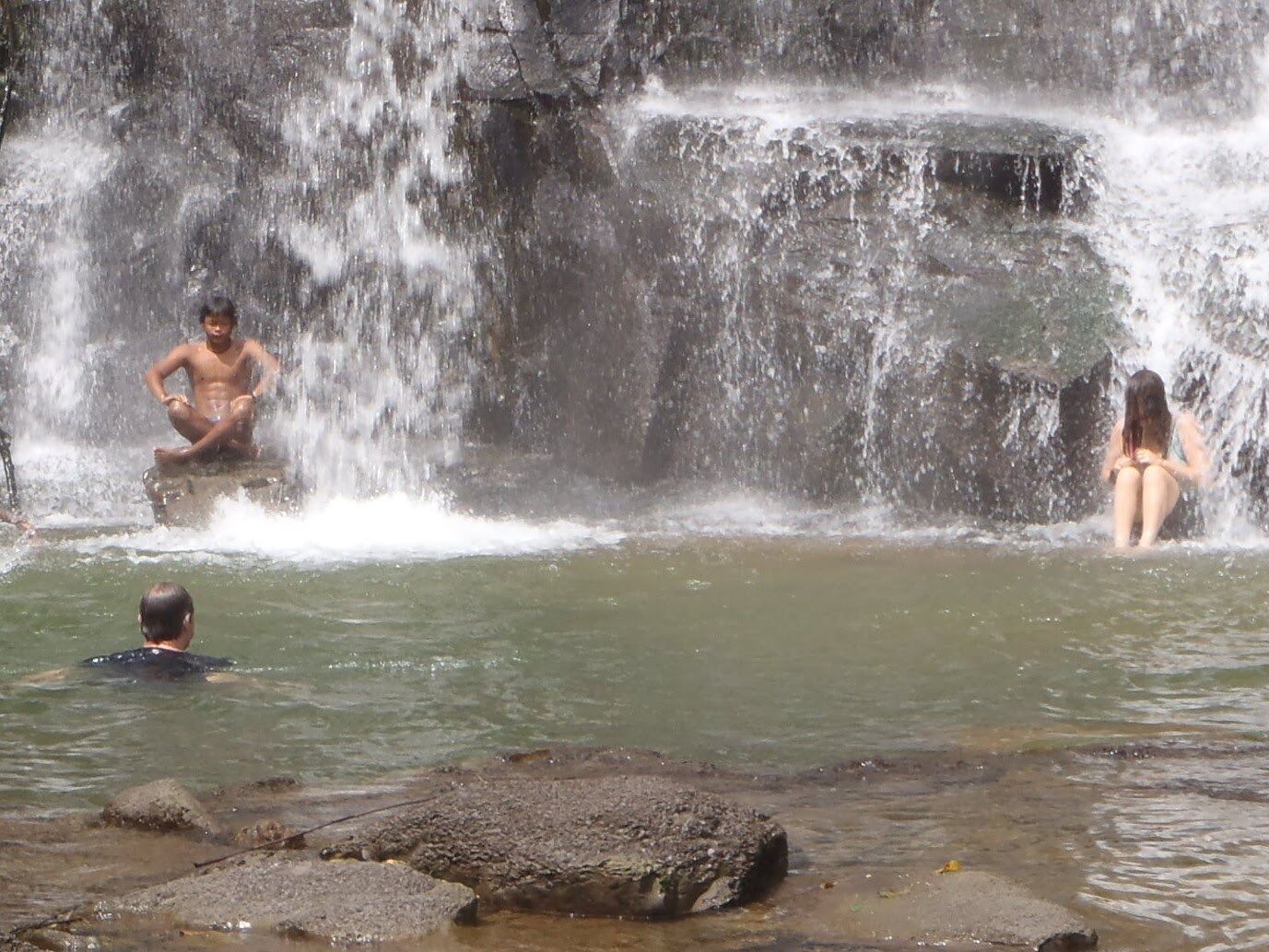 Una formación rocosa natural con cascada y personas disfrutando del agua.