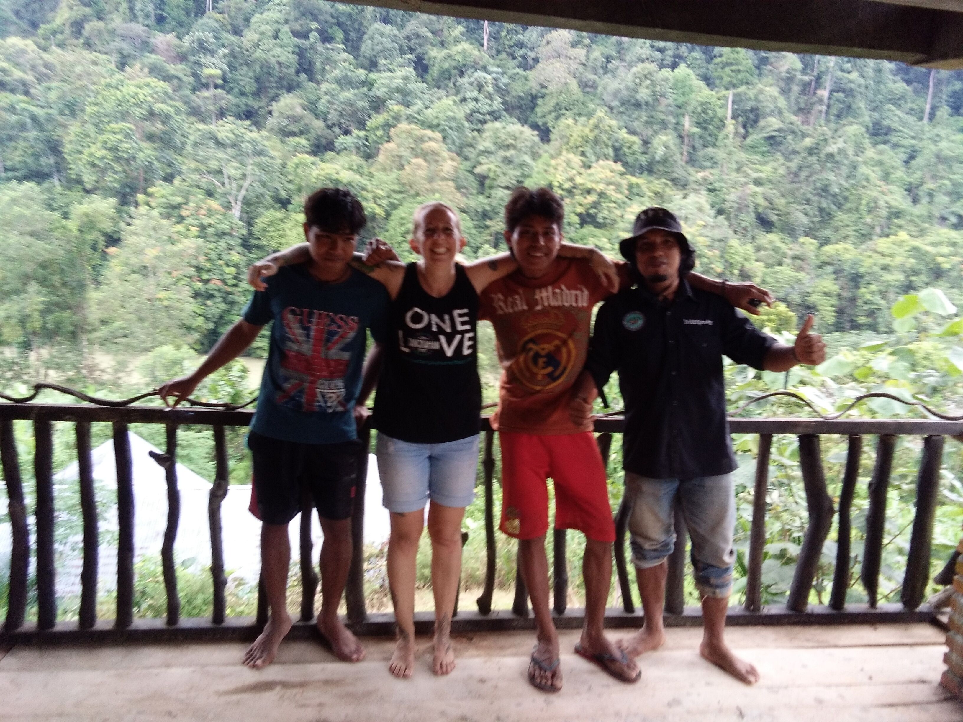 A group of people standing on a balcony with a forest view.