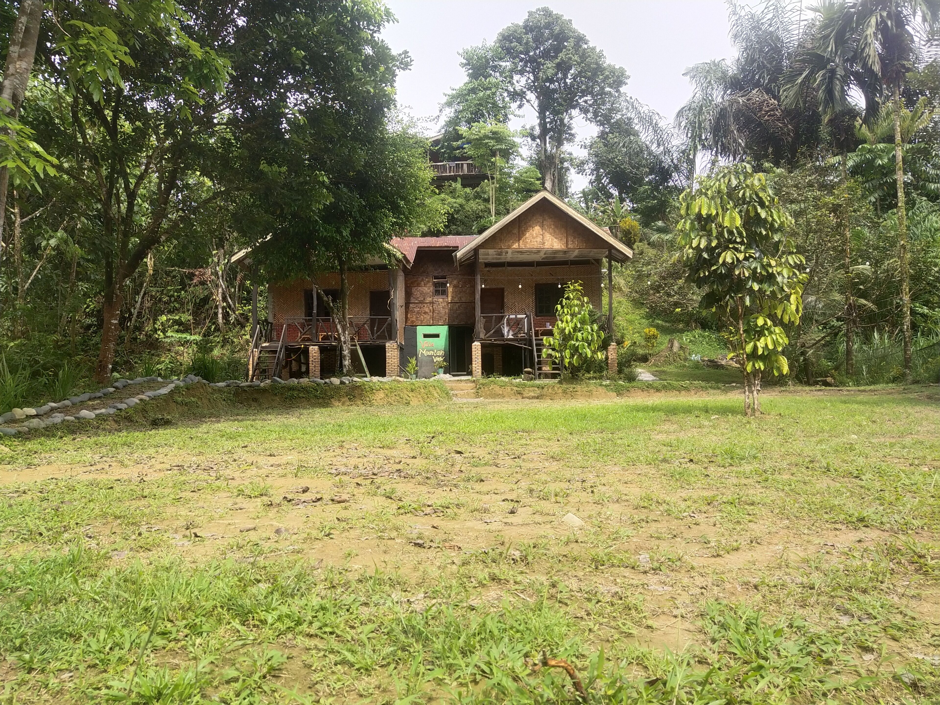 Une maison de campagne à l’aspect rustique, avec une façade en briques, un porche en bois et une porte verte.