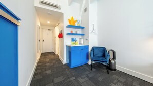 A hallway with a blue door, a blue cabinet with shelves, a blue chair, and a trash can.