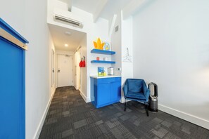 A hallway with a blue door, a blue cabinet with shelves, a blue chair, and a trash can. - The Gallatin (215) Colorful Boutique Hotel (Nashville)