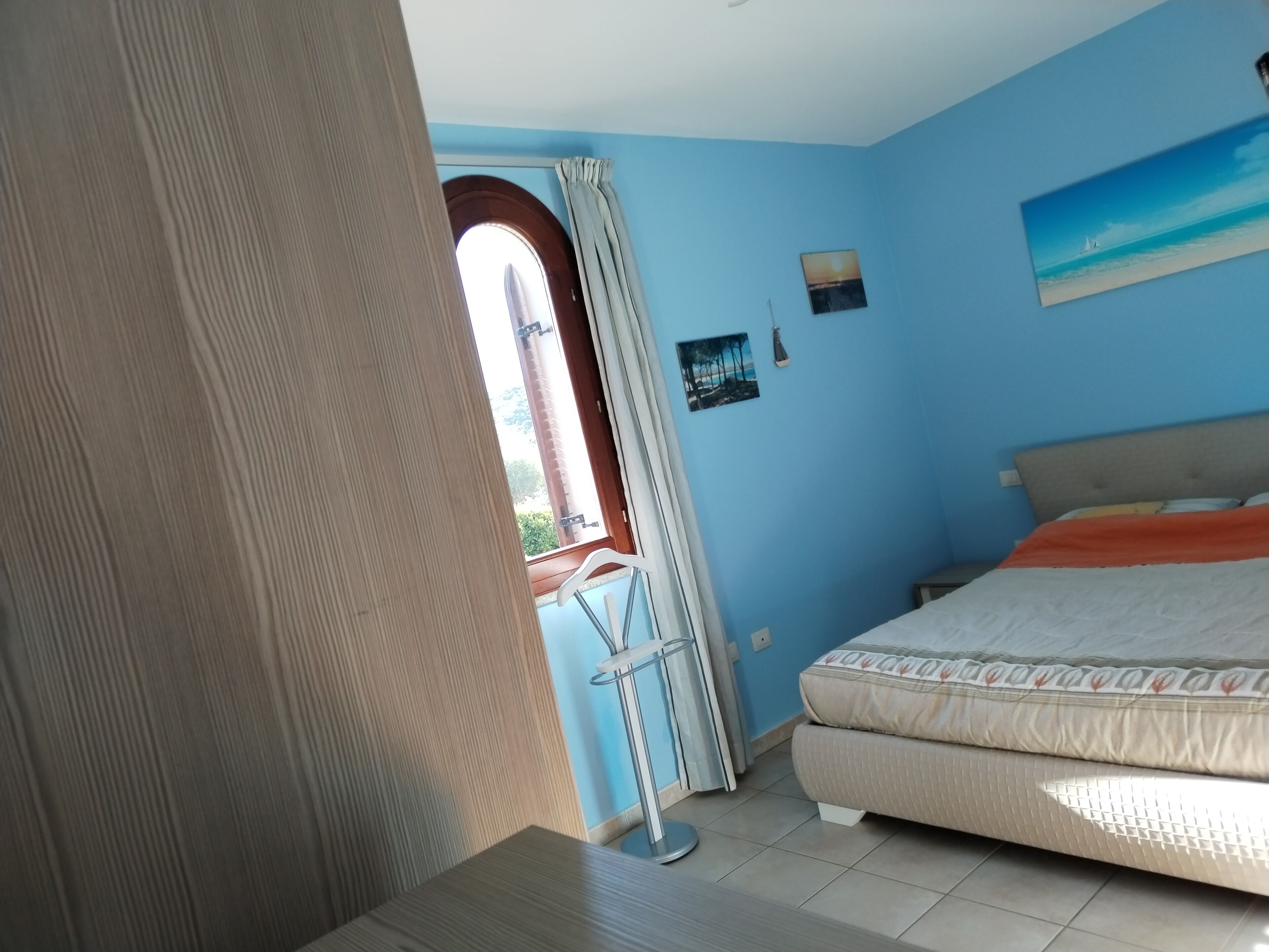 Una camera da letto con un letto, una finestra con tende, un quadro appeso al muro e una porta.