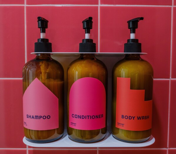 Three bottles of personal care products on a shelf against a red tiled wall.