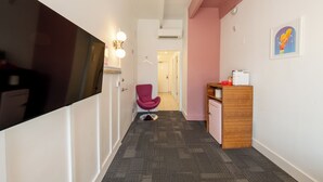 A hallway with a flat-screen TV, a pink chair, a wooden cabinet, and a framed picture on the wall.