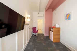 Un pasillo con una televisión de pantalla plana, un sillón rosa, un aparador de madera y un cuadro enmarcado en la pared.