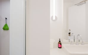 A bathroom with a white sink, a mirror, and a green bag hanging on the wall.