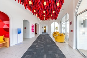A hotel lobby with a central carpeted walkway, red hanging decor, and a yellow sofa.