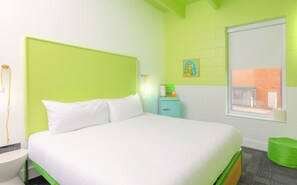 A hotel room with a bed, a nightstand, a small table, a green chair, a window, and a wall with a picture. - The Gallatin (217 Standard King) Hip Neighborhood! (Nashville)