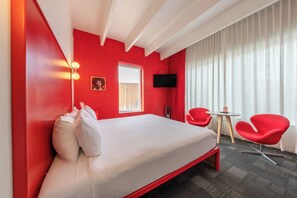 A hotel room with a bed, red walls, a window, a flat-screen TV, two red chairs, and a small table. - The Gallatin (219) Hip East Nashville Neighborhood! (Nashville)