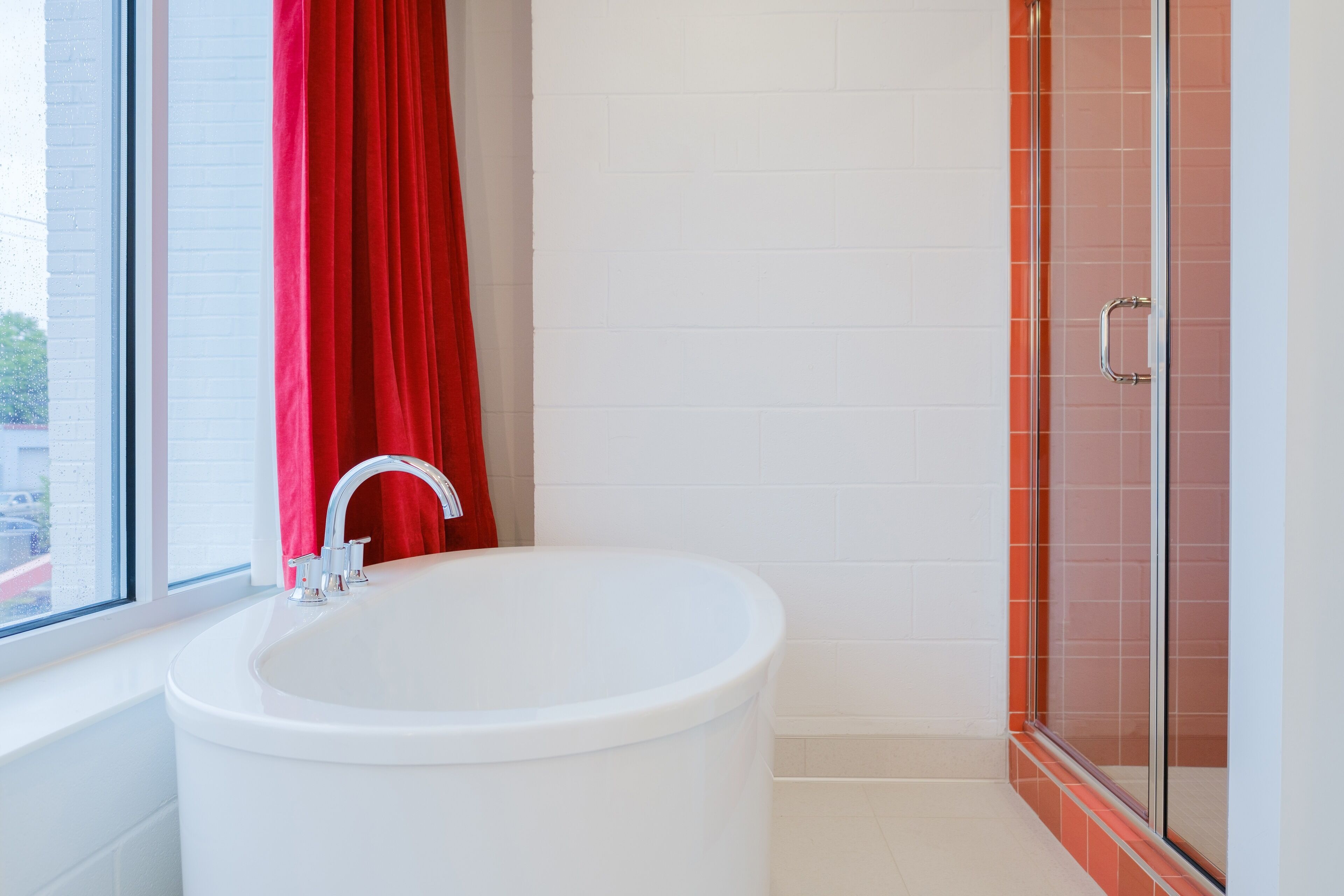 Ein Badezimmer mit einer weißen Badewanne, einem roten Vorhang und einer Duschkabine aus Glas.