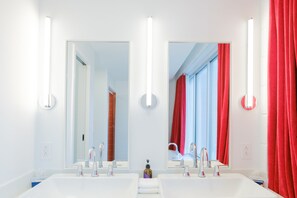 Une salle de bain moderne avec deux lavabos, un grand miroir et des rideaux rouges.