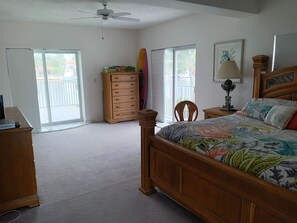 A bedroom with a wooden bed, a dresser, a ceiling fan, and a window with a view of the outdoors.