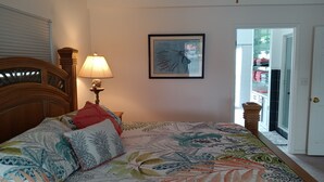 Een slaapkamer met een groot bed, een nachtkastje met een lamp, een ingelijste foto aan de muur en een deur naar de badkamer.