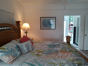 A bedroom with a large bed, a nightstand with a lamp, a framed picture on the wall, and a door leading to a bathroom. - Ocean View with protected dock on lagoon with private boat ramp (Islamorada)