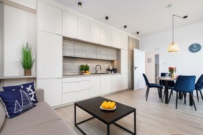 A modern kitchen with white cabinets, a dining area with blue chairs, and a coffee table with fruit. - Seaside Apartamenty Baltic Marina (Kolobrzeg)