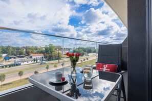 Un balcon avec une table, un vase rempli de roses rouges, un verre d’eau et une tasse.