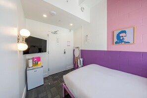 Un dormitorio con cama, un refrigerador pequeño, un espejo y una televisión instalada en la pared.