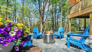 A deck with blue chairs and a fire pit, surrounded by trees and a flower arrangement.