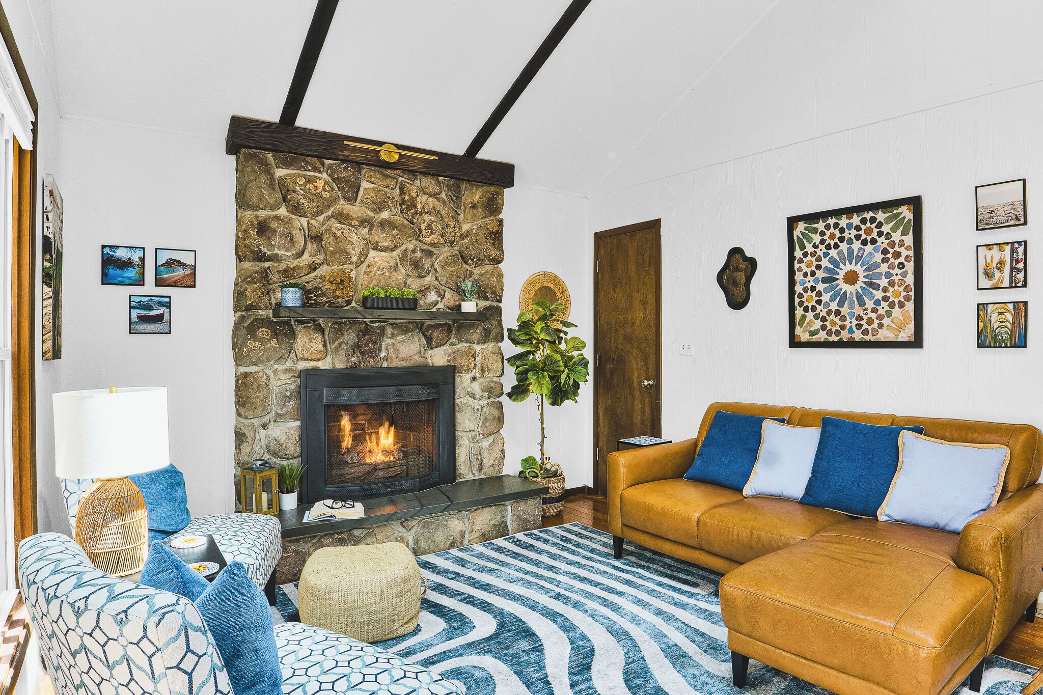 A living room with a stone fireplace, a sofa, a patterned rug, and wall art.