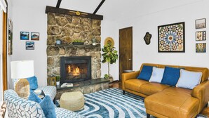 A living room with a stone fireplace, a sofa, a patterned rug, and wall art.