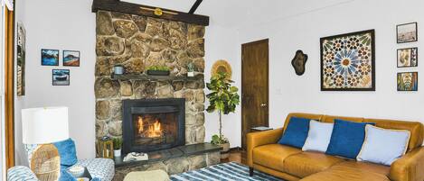 A living room with a stone fireplace, a sofa, a patterned rug, and wall art.