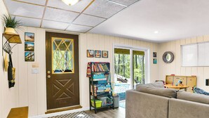 Un salon chaleureux avec une porte marron, une bibliothèque, un canapé et une fenêtre donnant sur un paysage naturel.