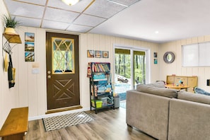 Una sala de estar acogedora con una puerta marrón, una estantería, un sofá y una ventana con vistas a un paisaje natural.