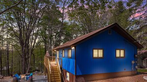 Une cabane bleue avec une terrasse en bois, un escalier et des sièges d’extérieur.