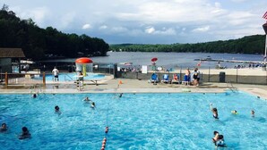A swimming pool with people in it, a lifeguard tower, and a view of the lake.