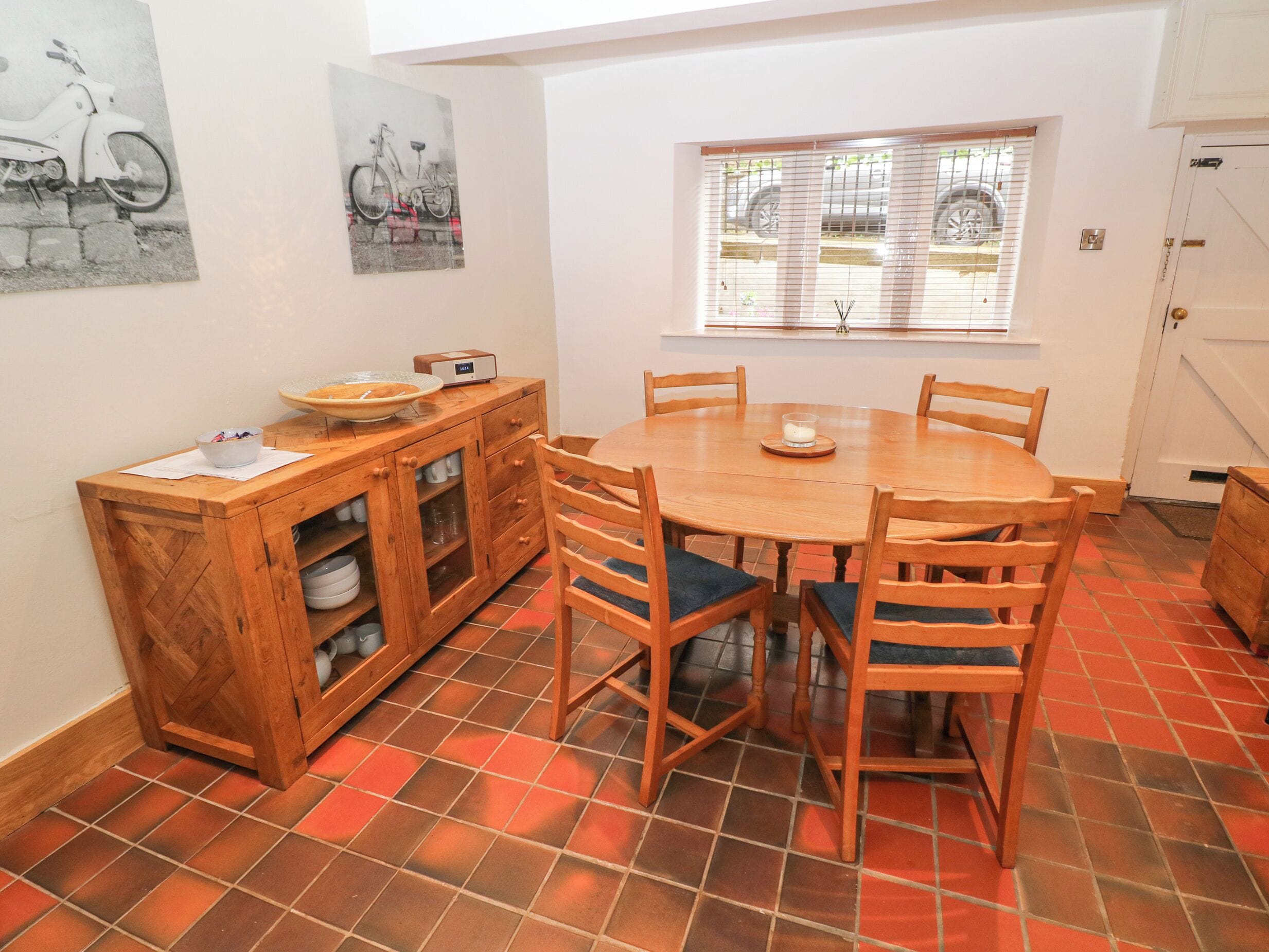 Un comedor con una mesa redonda de madera, seis sillas, un aparador de madera con puertas de vidrio y una ventana con persianas.