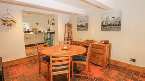 A dining area with a round wooden table and chairs, a wooden cabinet, and a tiled floor. - The Old Cobblers (High Peak)