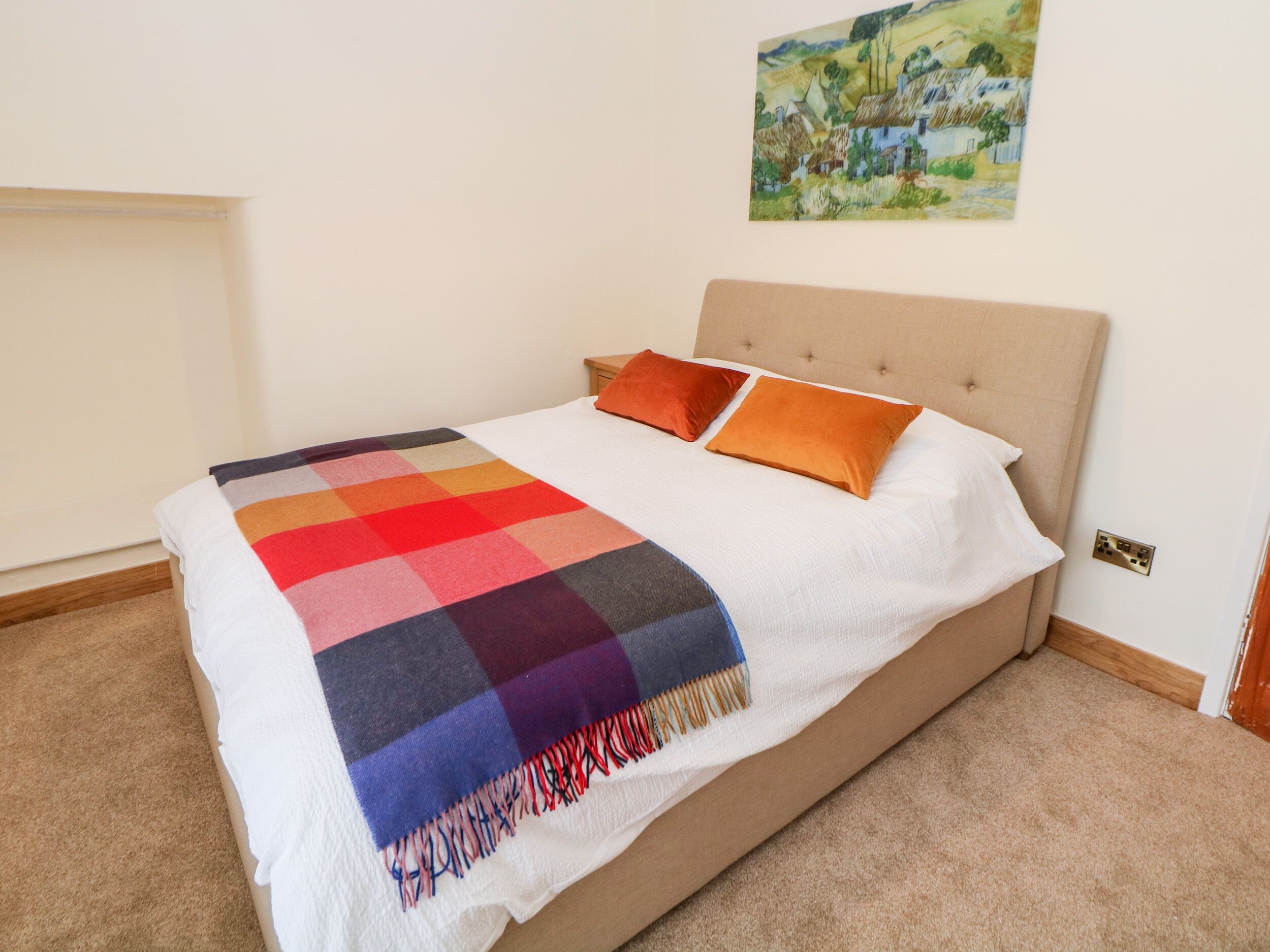 A bed with a colorful blanket, two pillows, and a painting on the wall.
