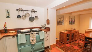 A kitchen with a vintage stove, hanging pots, and a dining area with wooden furniture. - The Old Cobblers (High Peak)