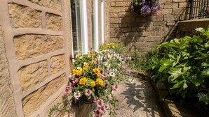 A stone building with a window and a flower planter on the right. - The Old Cobblers (High Peak)