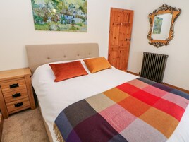Una cama bien hecha con una colcha colorida, una mesita de noche de madera con cajones, un armario de madera y un radiador.