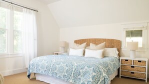 Een slaapkamer met een groot bed, twee nachtkastjes, een raam met gordijnen en een wit hoofdeinde.