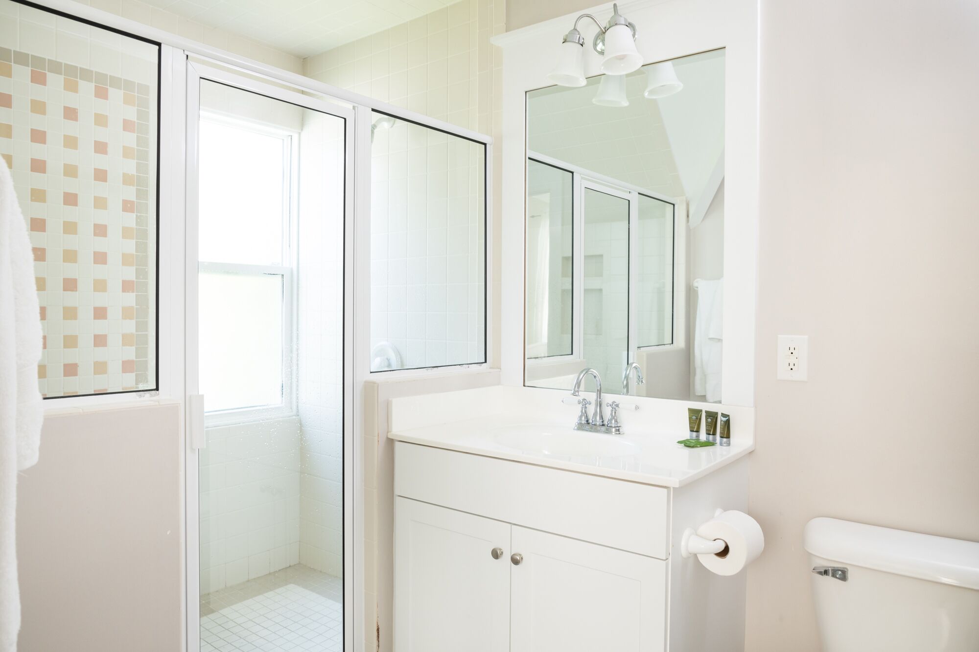 A bathroom with a white vanity, a large mirror, a toilet, and a shower area.