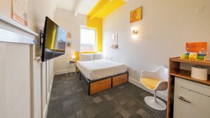 A hotel room with a bed, a TV, a desk with a chair, and a window. - The Gallatin (Standard Queen Room 314) Colorful Boutique Hotel (Nashville)