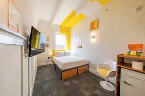 Ein Hotelzimmer mit Bett, Fernseher, Schreibtisch mit Stuhl und Fenster.