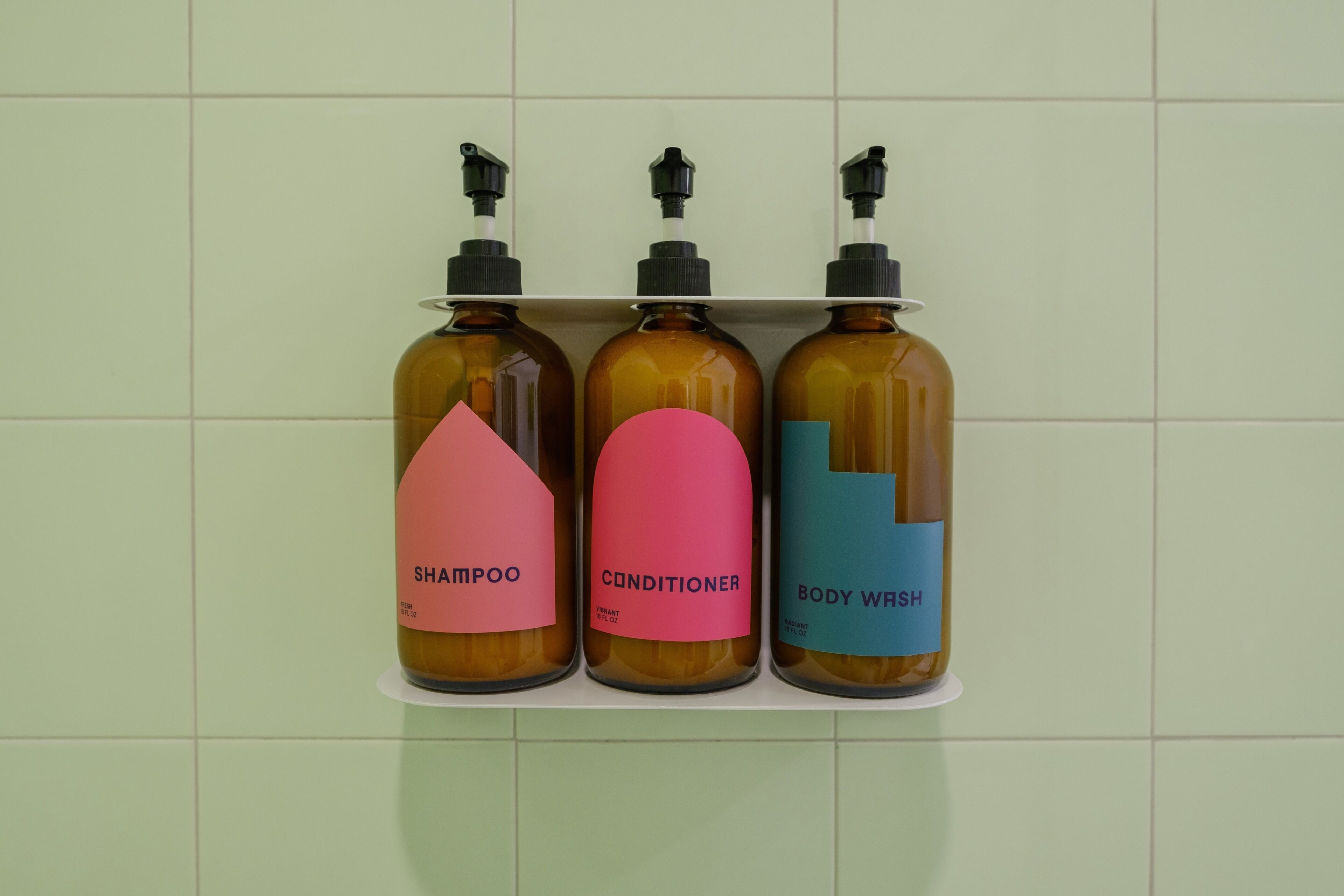 Drie flessen shampoo, conditioner en douchegel op een plank.